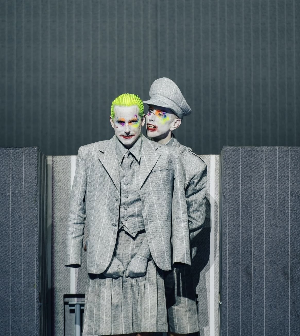 Two performers in grey pinstripe suits with painted faces