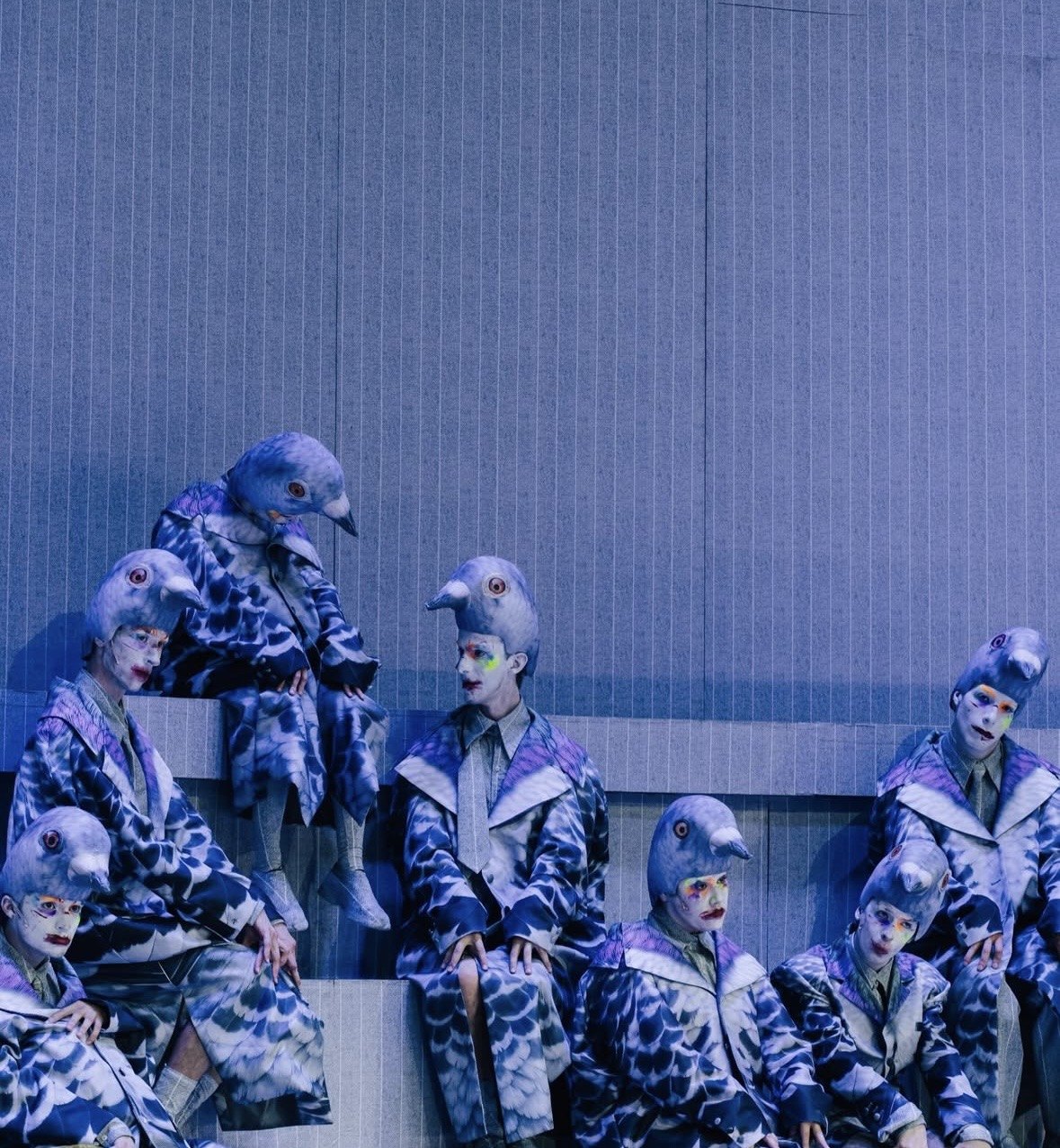 Chorus dressed as pigeons sitting on grey steps